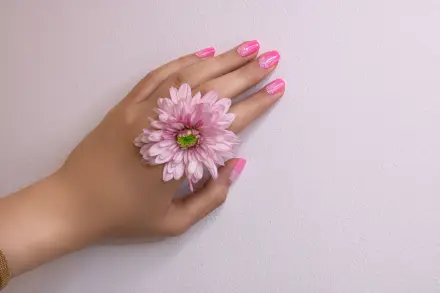 Mano con uñas rosas sujetando una flor rosa